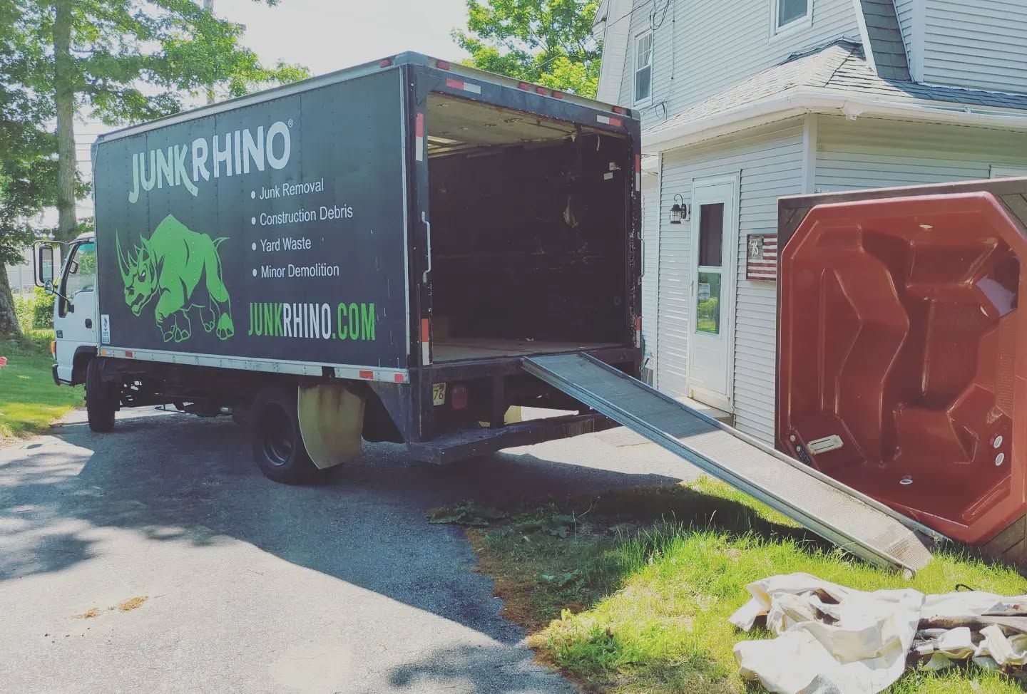 A Junk Rhino truck with an open ramp next to a red hot tub. The truck is parked in a residential driveway.