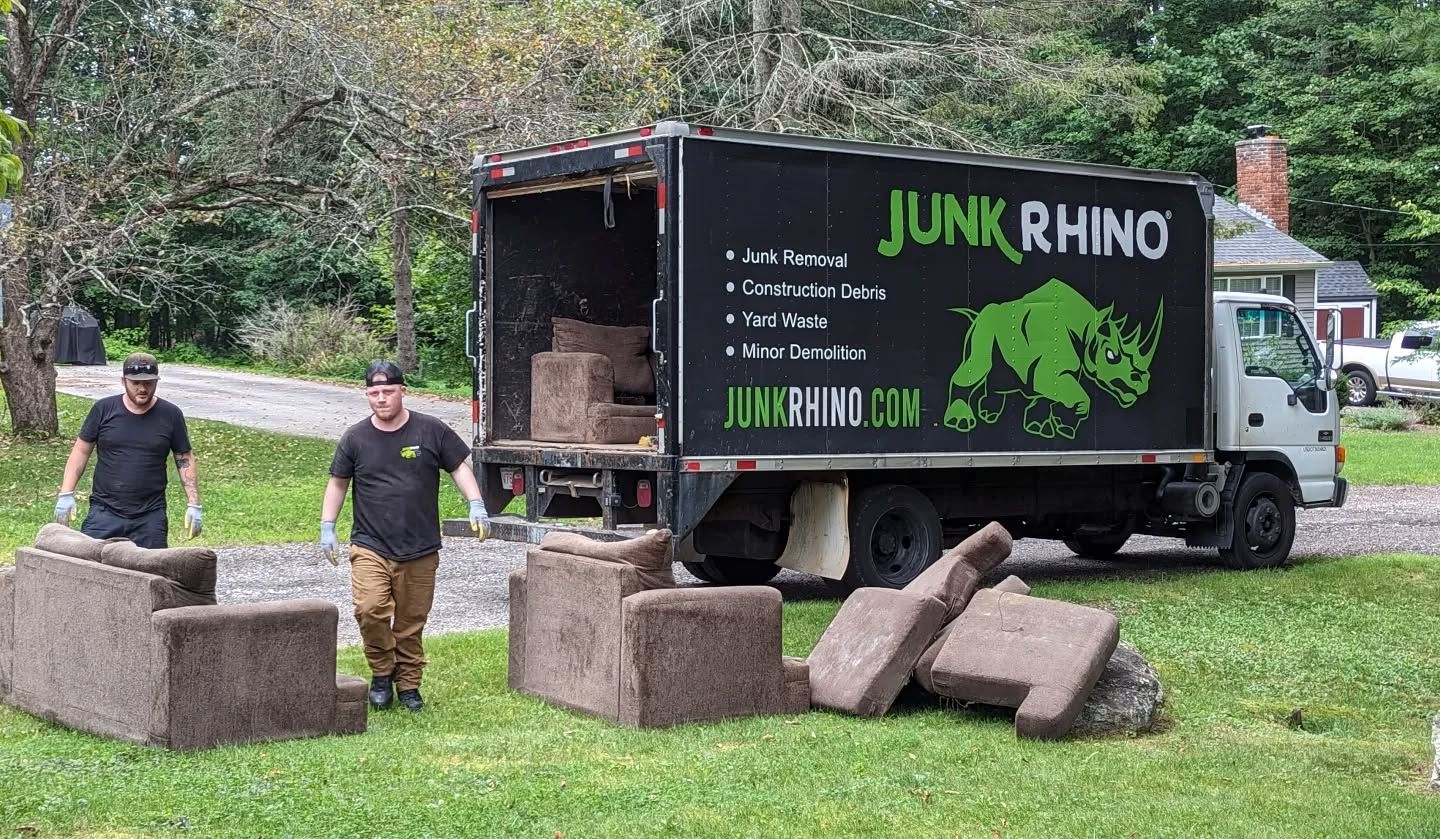 Two men loading furniture into a Junk Rhino truck on a grassy lawn.
