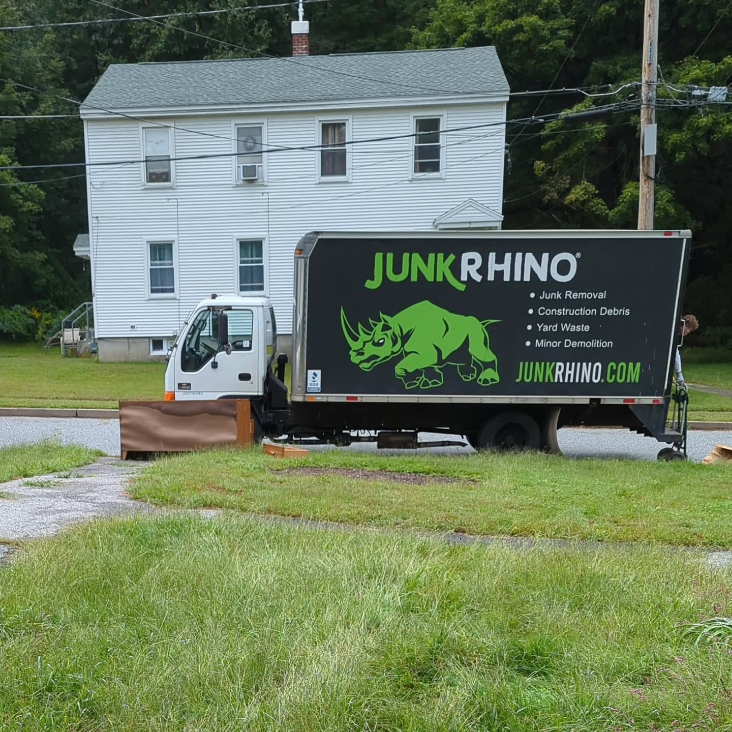 Junk removal truck parked in front of a white house with grass and trees.