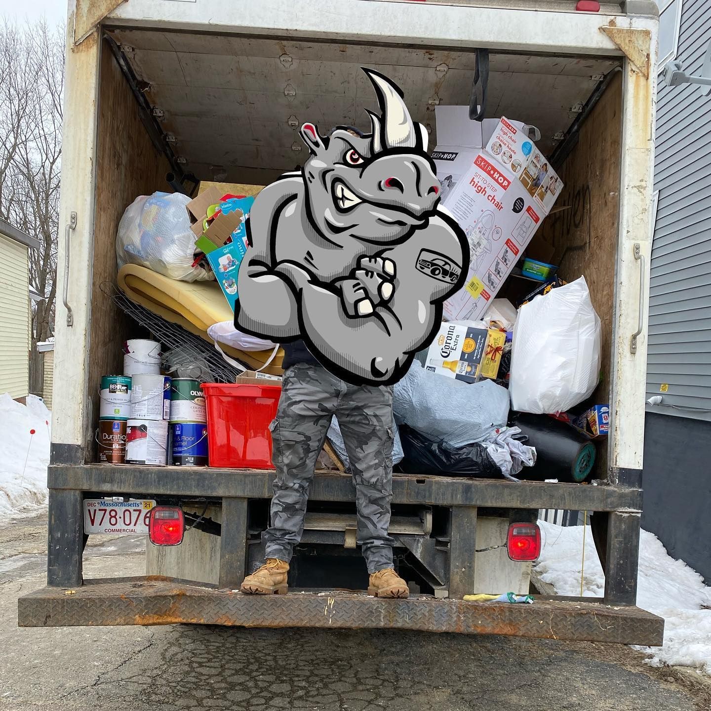 A person in camo pants and a rhino logo overlay stands in front of a truck loaded with household items.