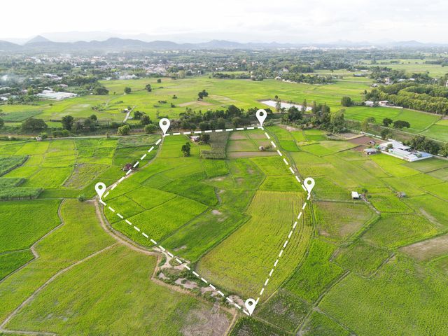 Aerial view of green fields marked with location pins, outlining a plot of land with a town in the distance.