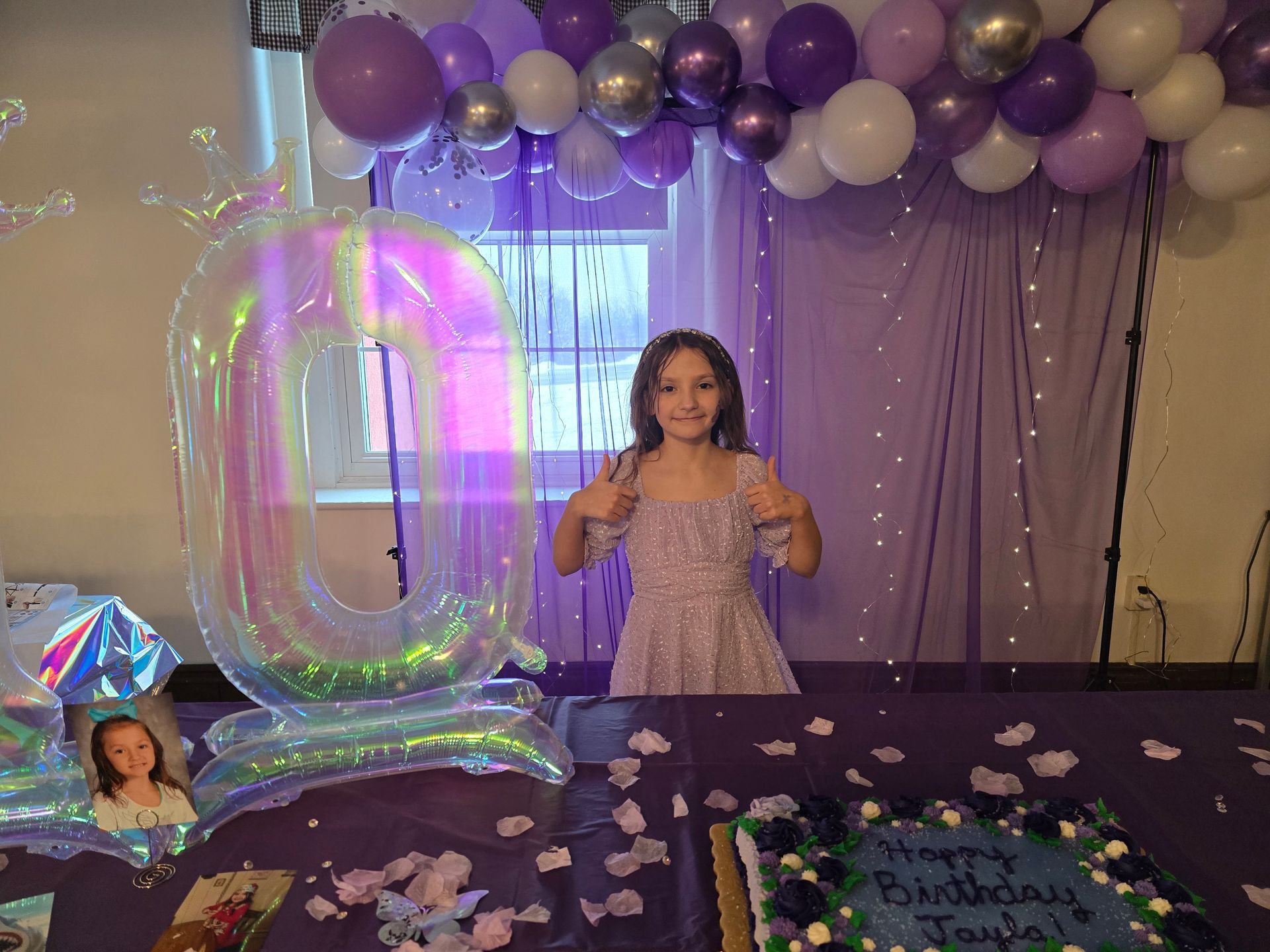 A girl poses in front of a purple birthday display with a large number 10 balloon and a cake labeled 
