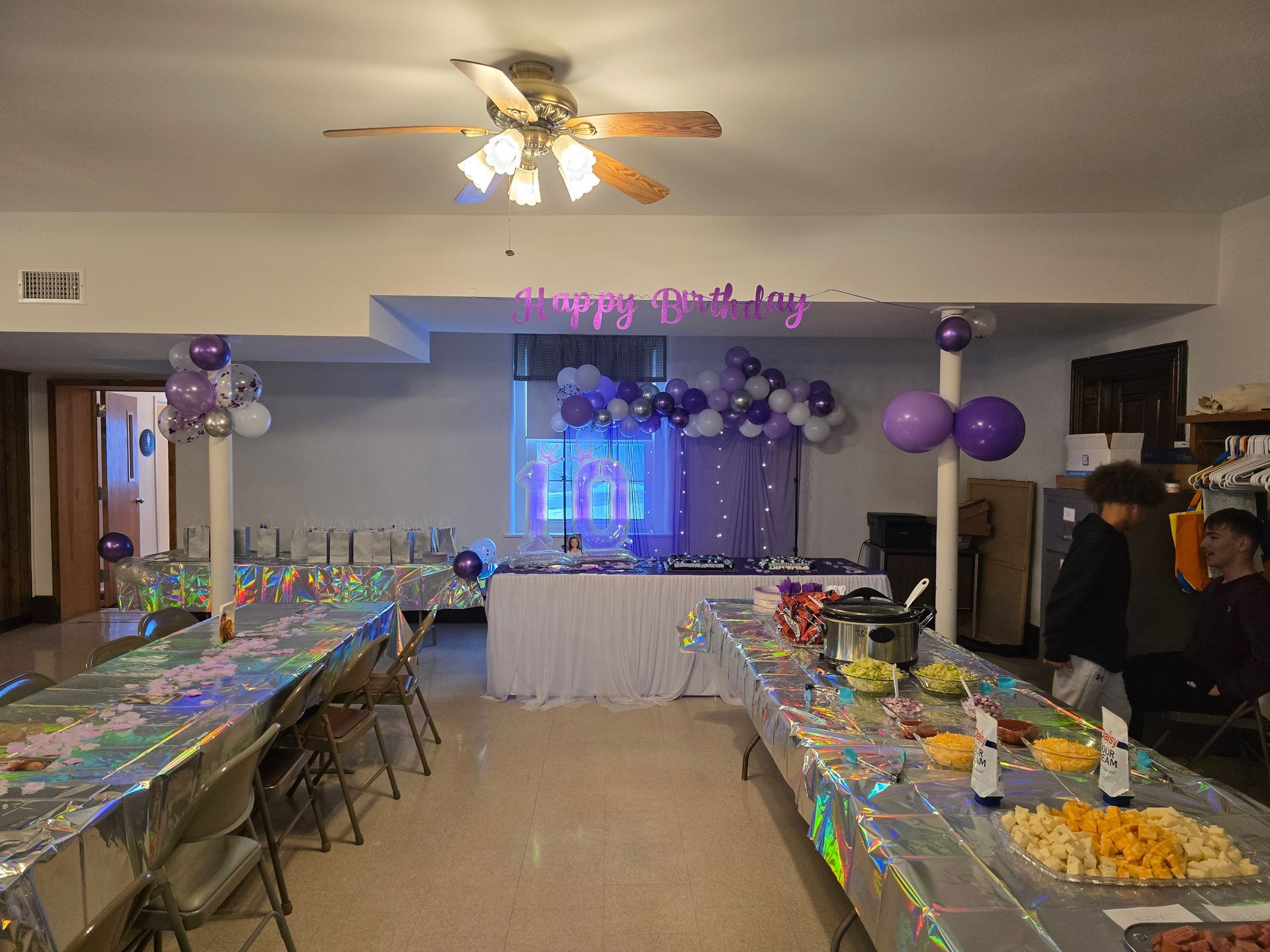 A long dining table set for an event with blue napkins, glassware, and sunflower floral arrangements.