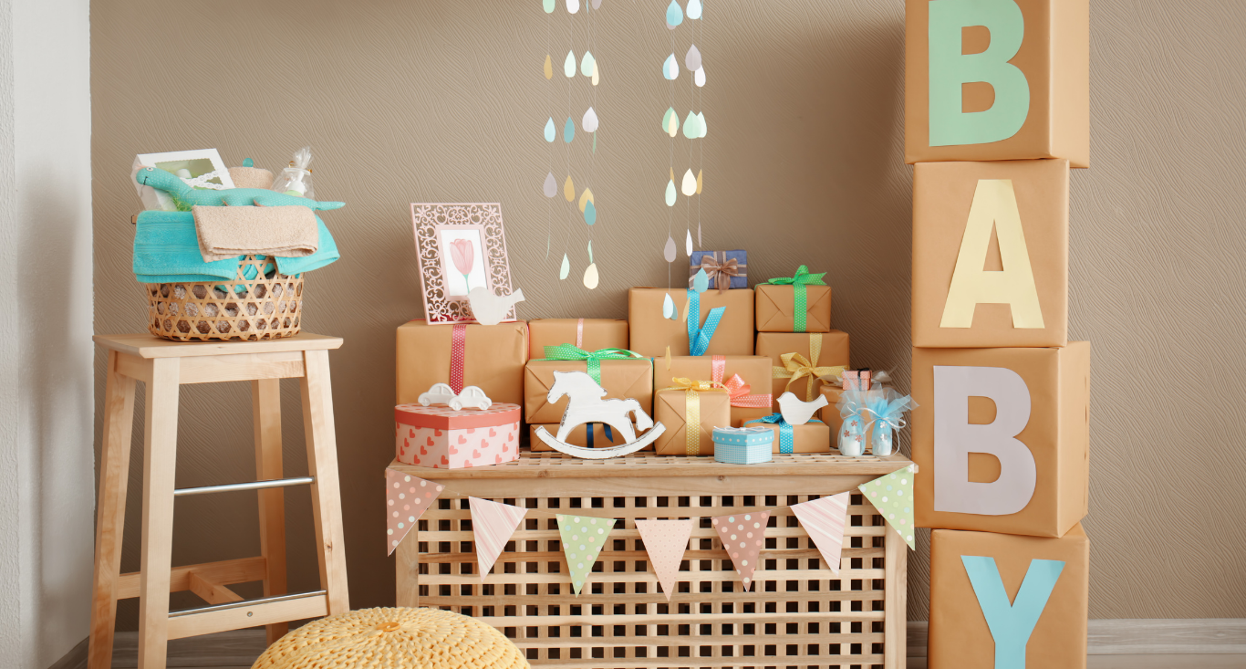 Baby shower decor with a wooden stool, gifts on a lattice table, and stacked boxes spelling 