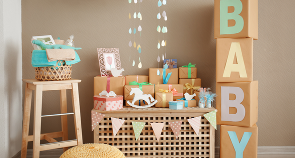 Baby shower decorations featuring a wooden stool, gifts on a table, and a stack of boxes spelling 