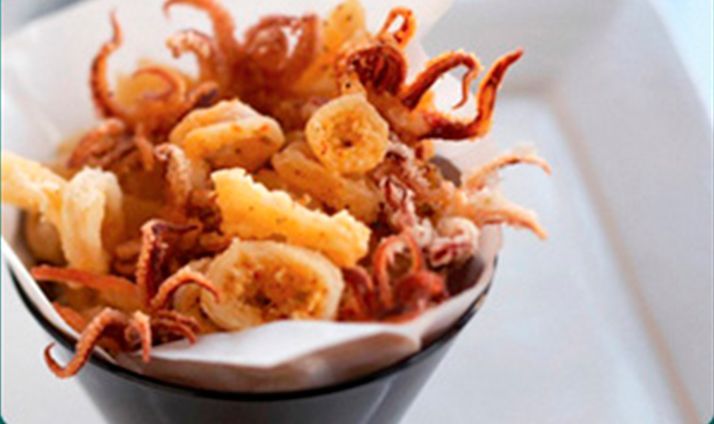 Calamares fritos en cono negro, con tentáculos y aros dorados, con revestimiento de papel blanco.