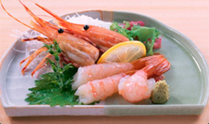 Sashimi de camarones en plato con limón, wasabi y guarnición.