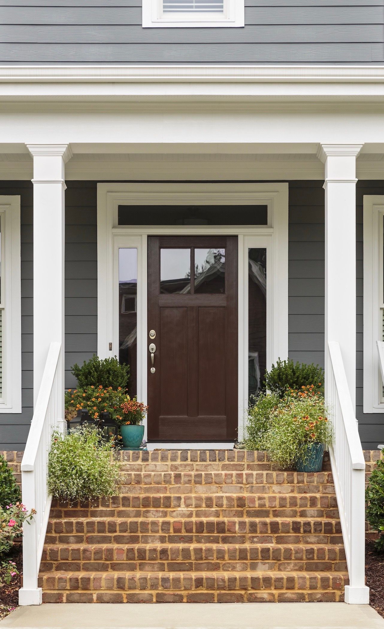 Front entry of a gray house with brick steps, white columns, and a dark brown door