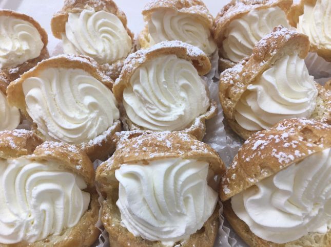 A bunch of cream puffs with whipped cream and powdered sugar on them