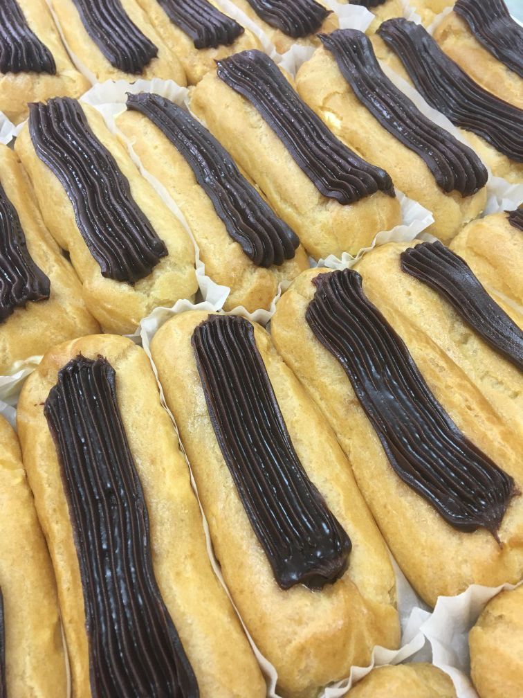 A close up of a tray of eclairs with chocolate frosting.