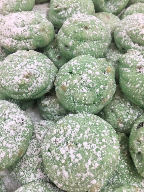 A pile of green cookies covered in powdered sugar on a table.