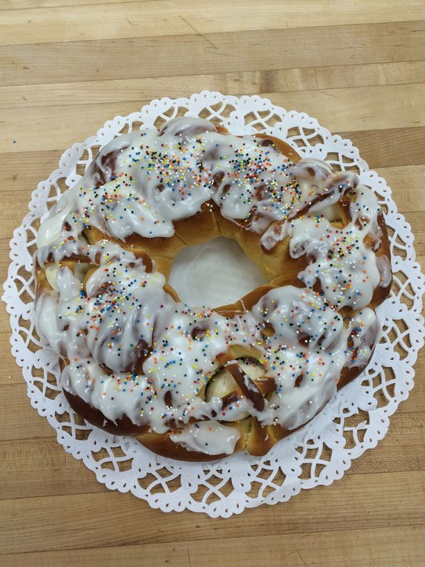 A cinnamon ring with icing and sprinkles on a napkin on a wooden table.
