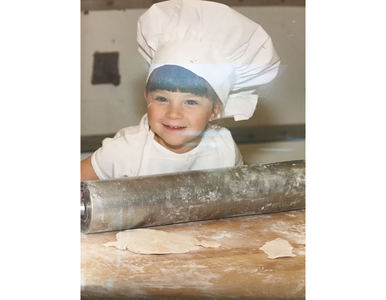 A young boy wearing a chef 's hat is rolling dough with a rolling pin.