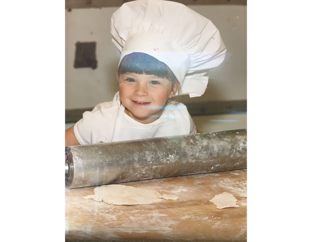 A young boy wearing a chef 's hat is rolling dough with a rolling pin.