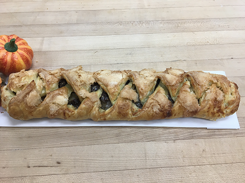 A long pastry is sitting on a wooden table next to a pumpkin.