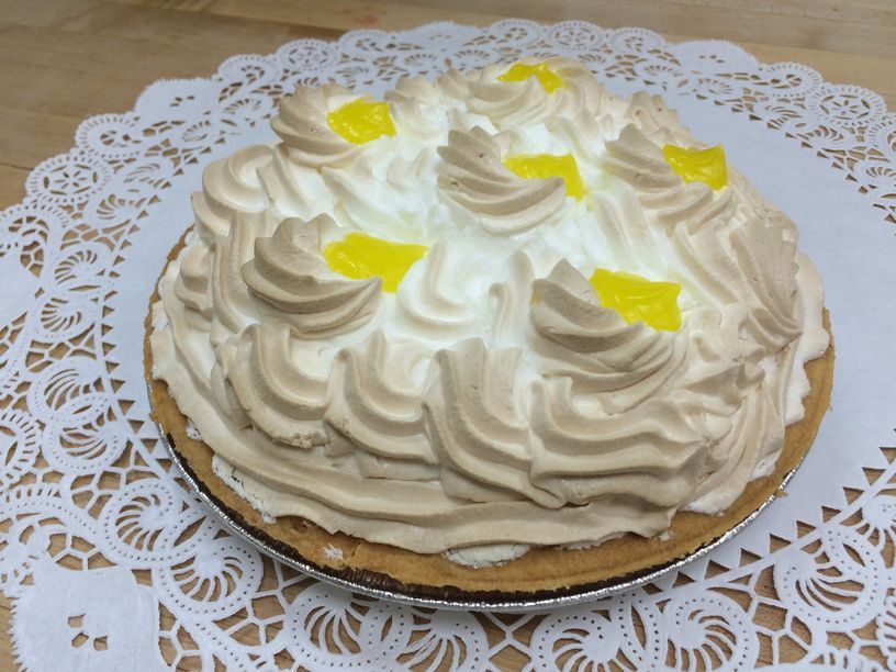 A lemon meringue pie is sitting on a lace napkin on a table.