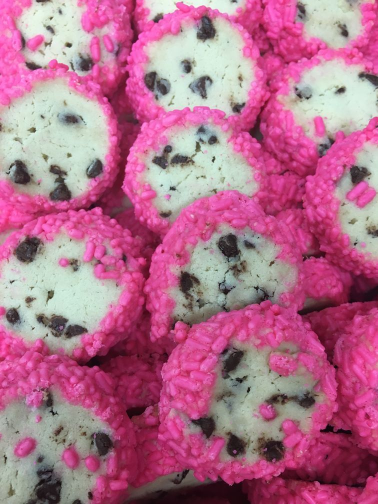 A close up of a pile of cookies with pink frosting and chocolate chips.