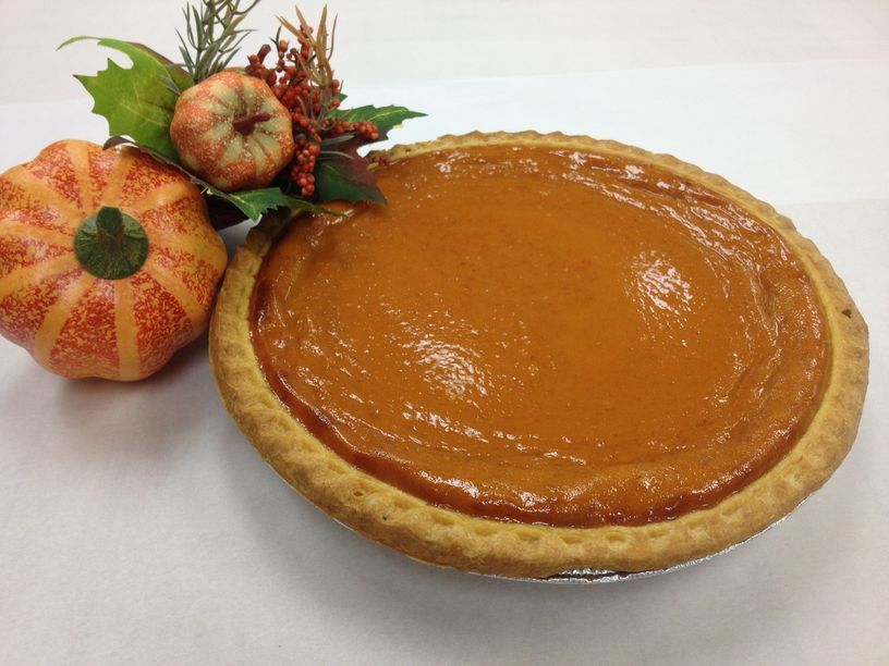 A pumpkin pie is sitting next to a fake pumpkin on a table.