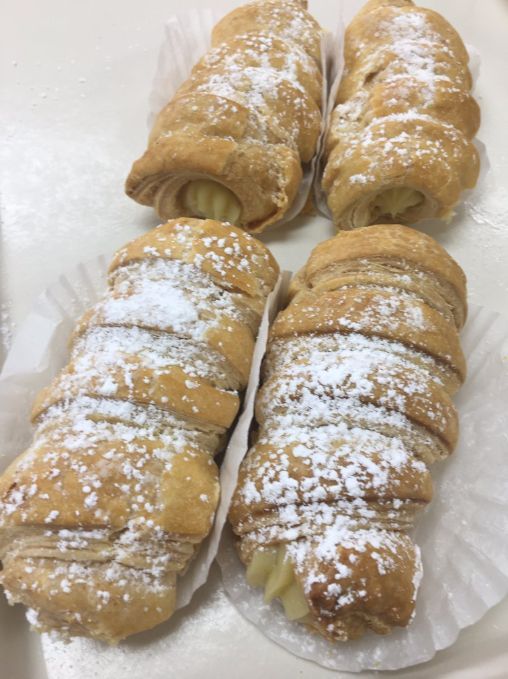 A close up of four pastry rolls with powdered sugar on a tray.