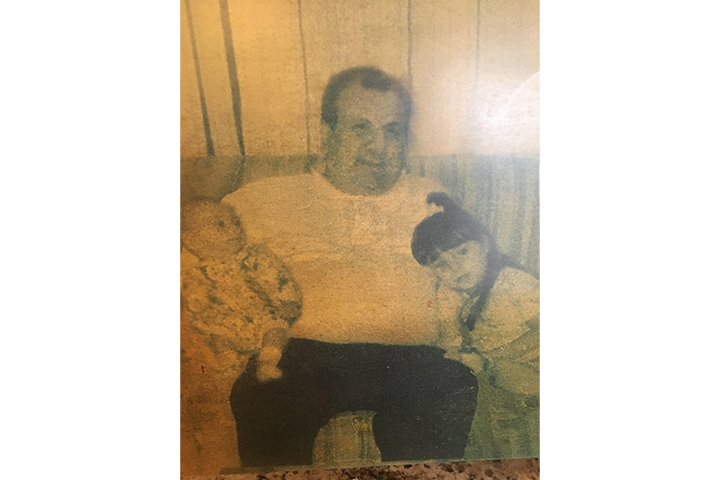 A man is sitting on a couch holding a baby and a little girl.