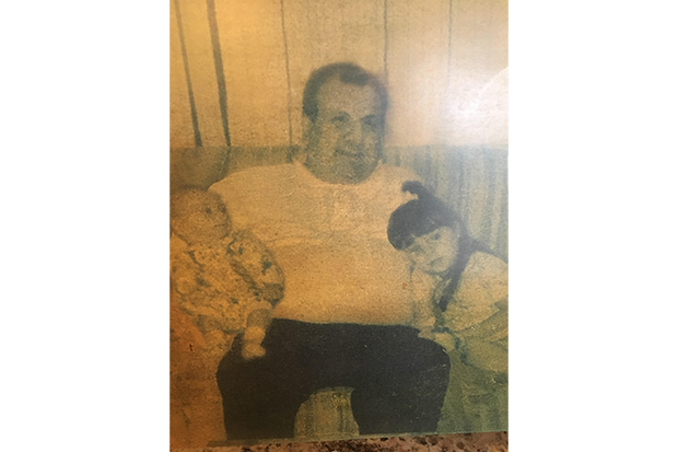A man is sitting on a couch holding a baby and a little girl.