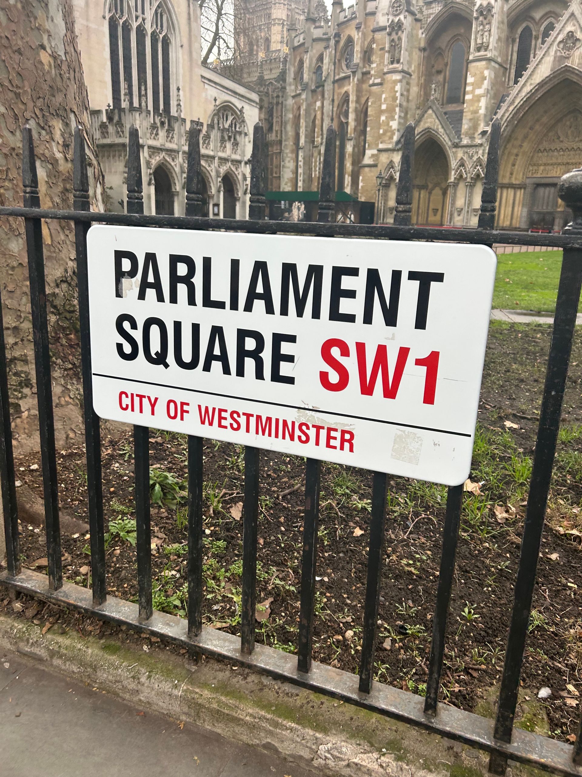 A sign reading Parliament Square SW1 City of Westminster hanging on a black fence