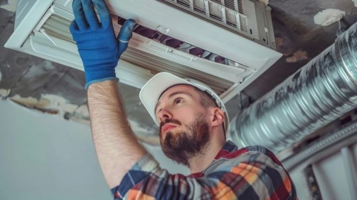 A man in a white hat is cleaning the ductwork.