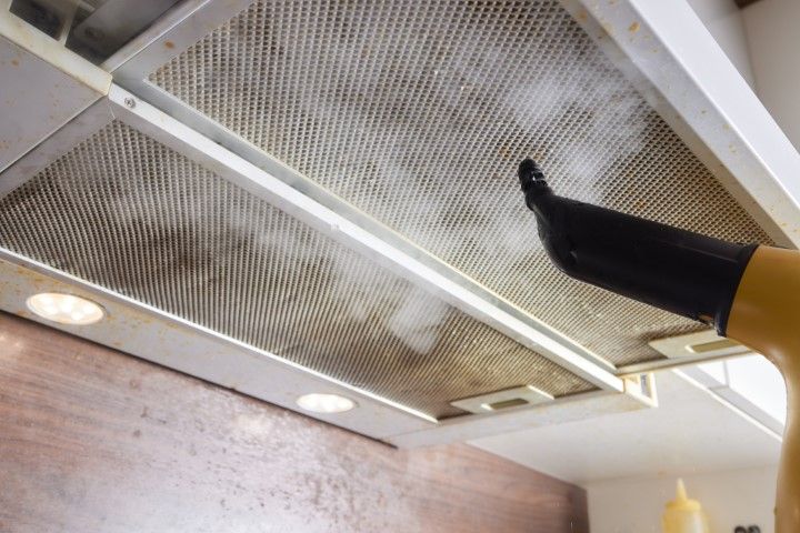 A dirty kitchen hood is being cleaned using a machine.
