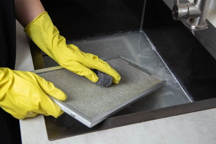 A worker wearing a yellow glove while cleaning the kitchen hood of the exhaust.