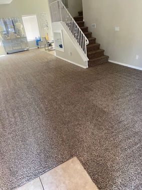 Brown carpeted living room with stairs and a window.