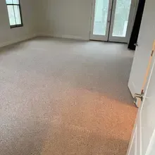 Beige carpeted room, with a window on the left and a door on the right. French doors in the background.