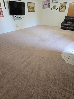 A spacious living room with tan carpet, a TV, and leather couch.