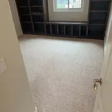Empty room with beige carpet, built-in dark wood shelves and window seat, and small window.