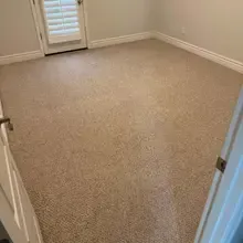 Empty room with tan carpet and white door and trim; shuttered door to outside.
