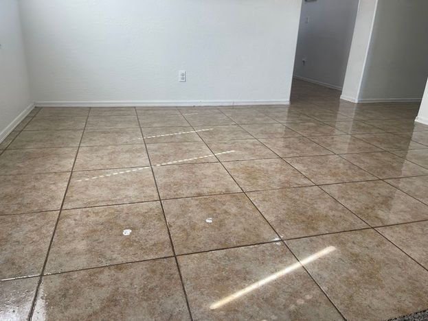 Empty room with light-brown tile flooring and white walls. Sunlight reflects on the floor.