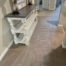Wooden console table with gray top and white legs in a hallway with beige carpet.