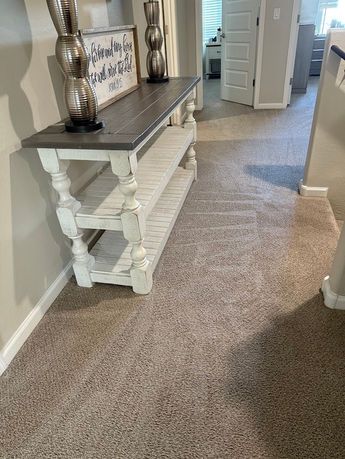 A console table with a gray top and white base sits on a carpeted hallway.