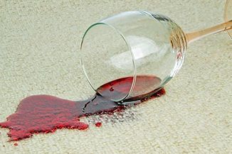 Spilled red wine on a beige carpet with a tipped-over wine glass.