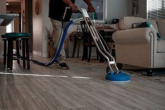 Person cleaning tile floor with a blue circular machine in a living room.
