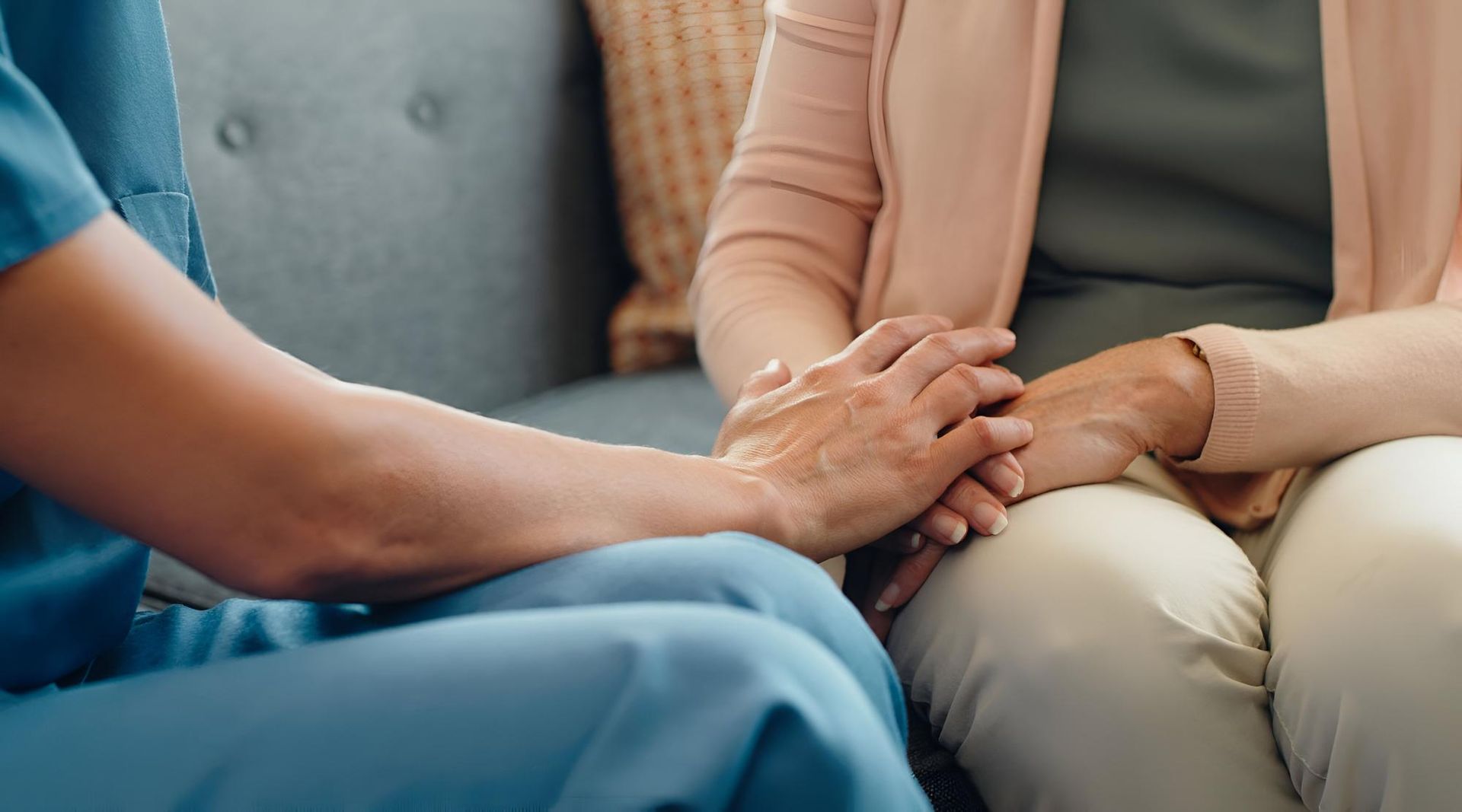 A nurse is holding the hands of an elderly woman on a couch.
