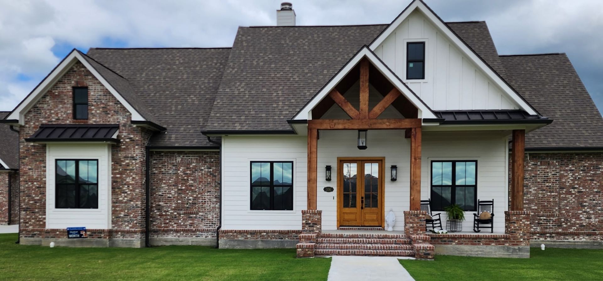 A single-story suburban house with white siding, brick accents, a dark roof, and a wooden porch entry.