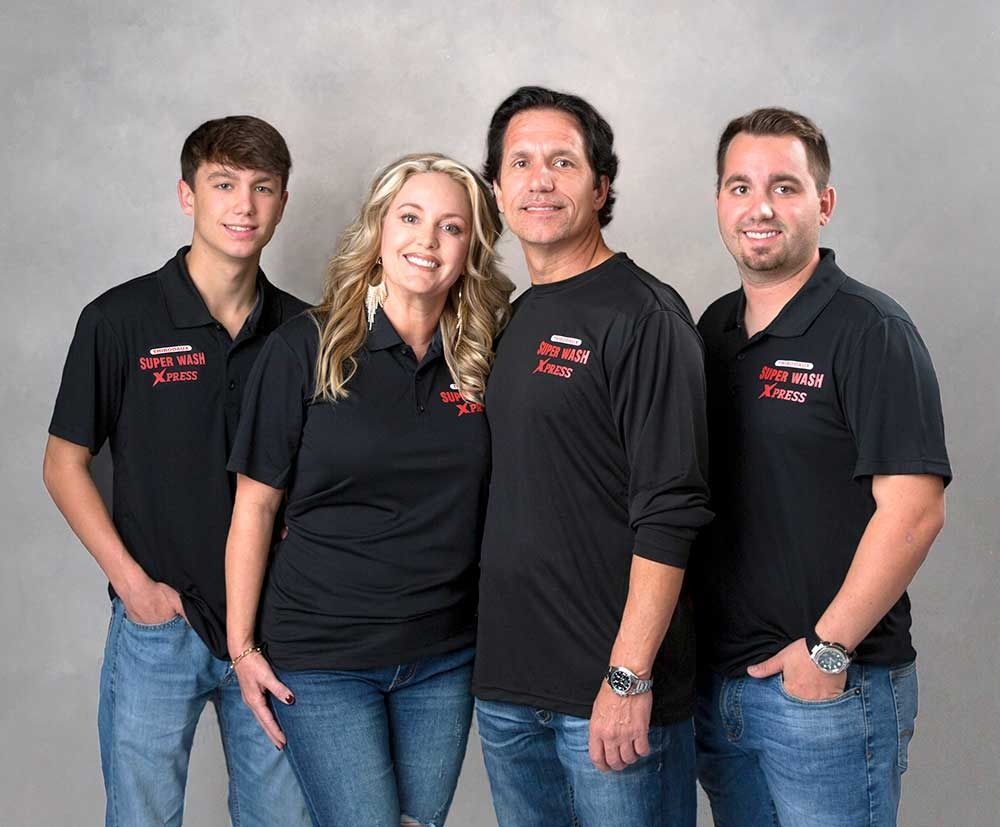 Four people wearing matching black polo shirts and jeans pose against a light gray background.