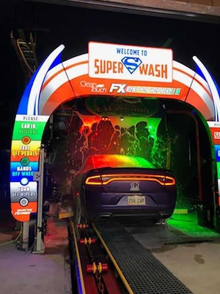 A purple Dodge Charger enters a brightly lit Super Wash car wash tunnel with colorful neon lighting.