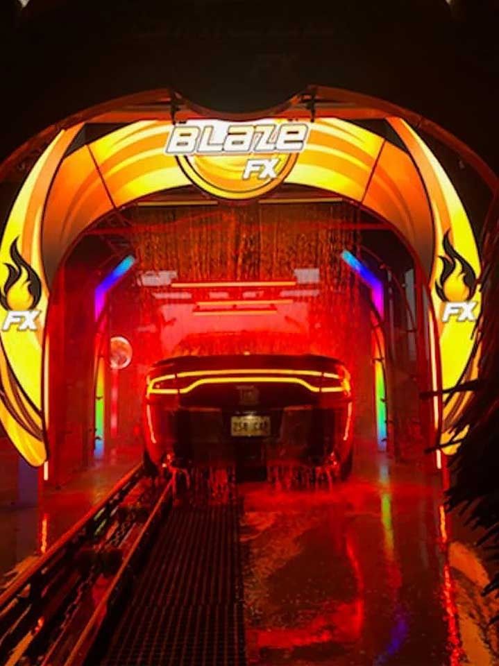 A dark car enters a brightly lit "Blaze FX" car wash, surrounded by vibrant red, orange, and blue LED lighting.