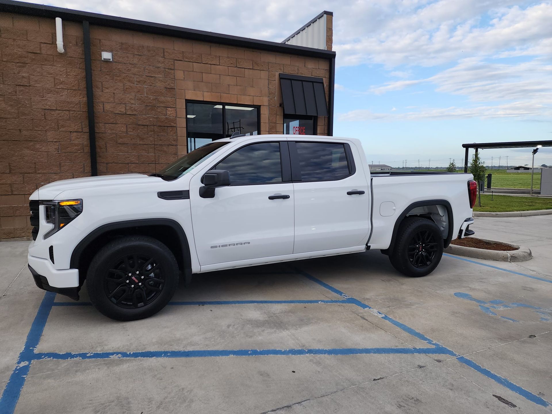 A white GMC Sierra pickup truck parked in a handicapped spot next to a brick building.