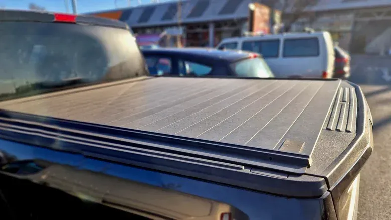 A silver crew cab pickup truck parked in a marked parking spot in front of a tan brick building.