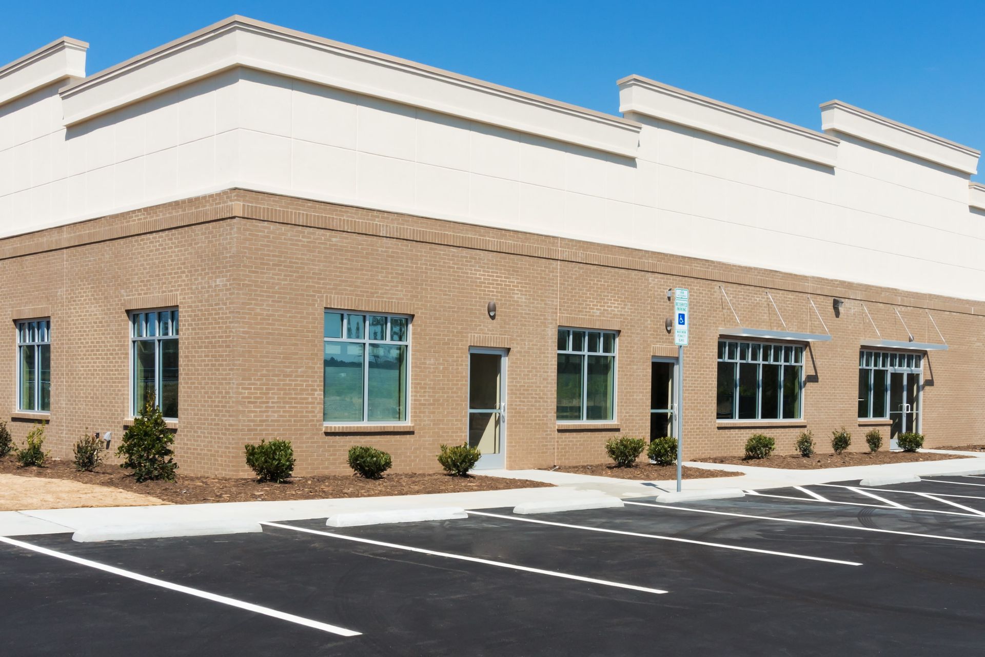 A modern single-story commercial building with tan brick, a white upper facade, and multiple entry doors and windows.