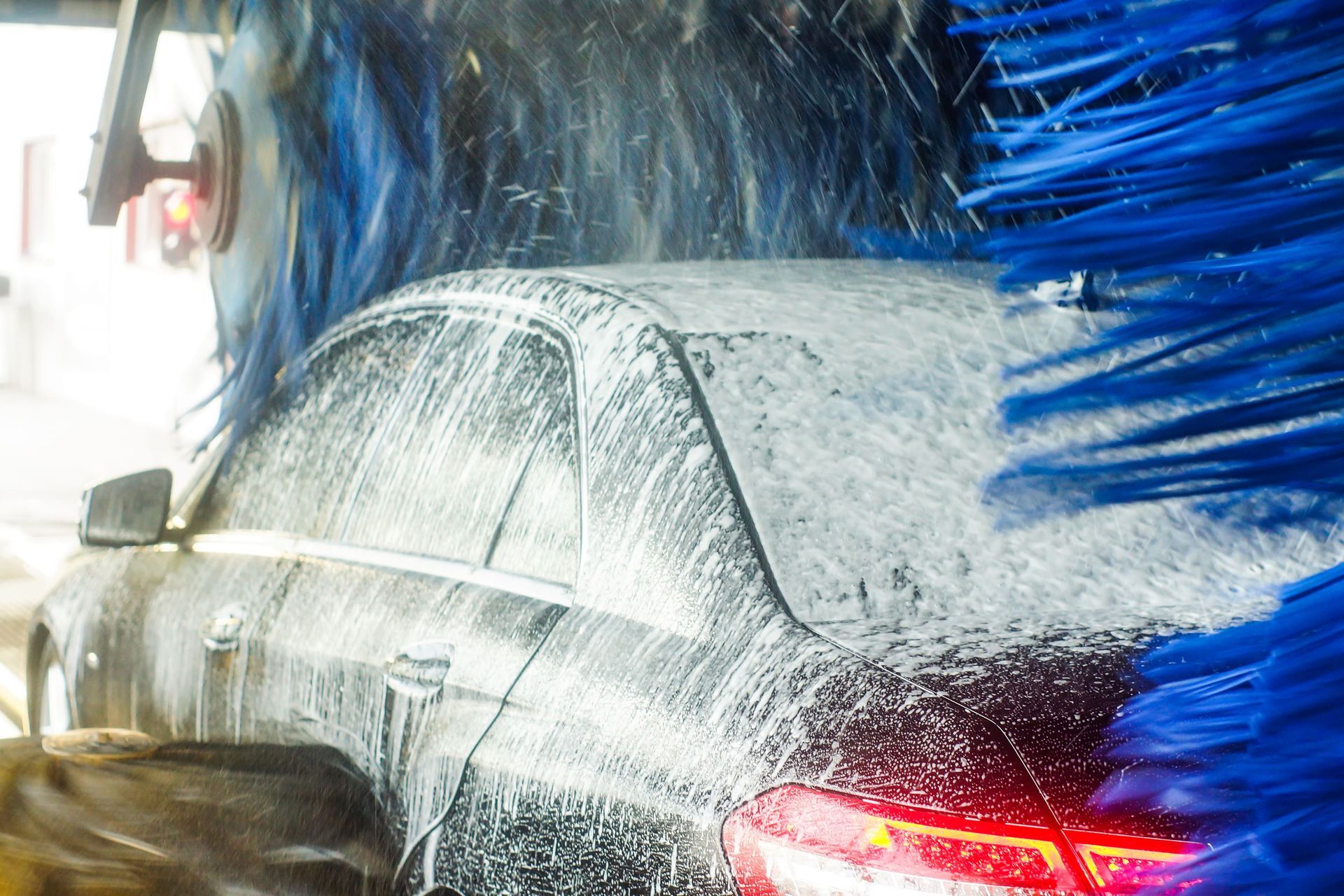 A car covered in soap suds passes through a car wash, with blue brushes spinning around it.