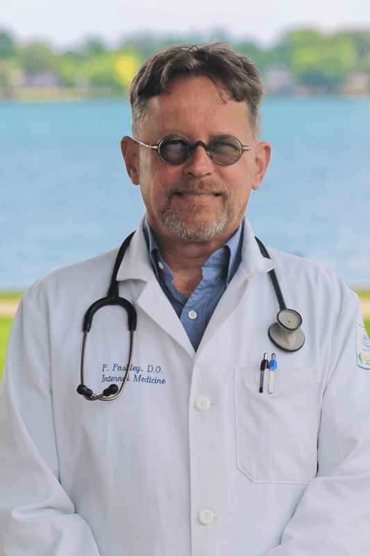 A doctor with a stethoscope around his neck is standing in front of a body of water.