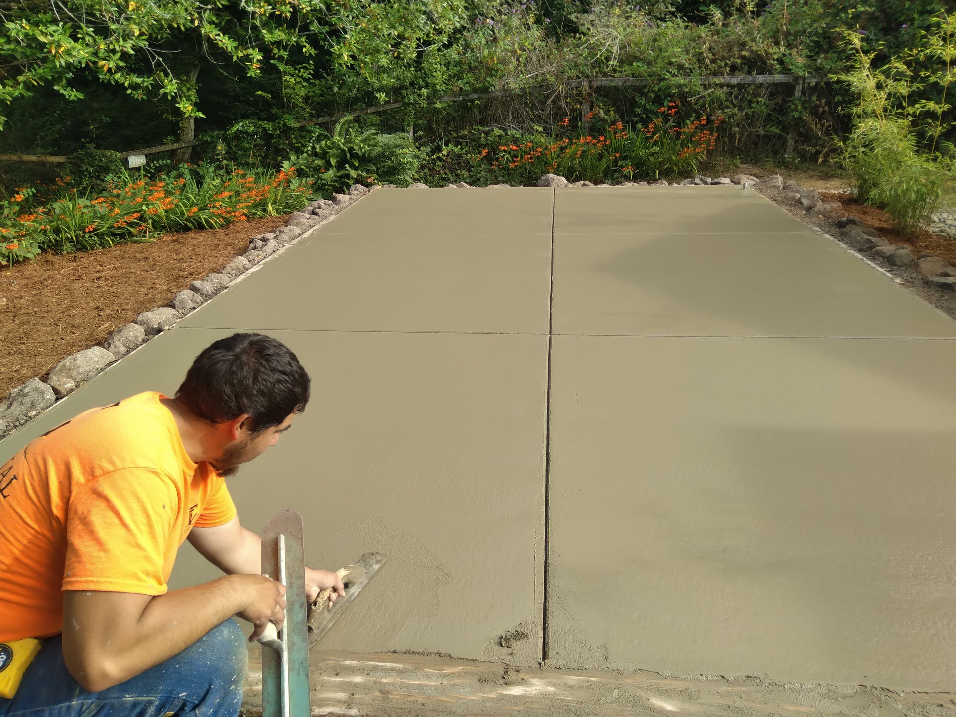 Person building a roof outdoors; wearing yellow shirt, jeans, and white shoes; among trees.